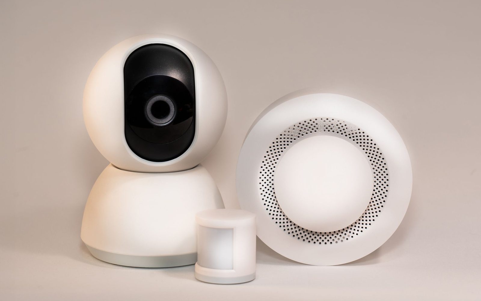Wireless alarm camera, movement sensor and sounder on a plain background